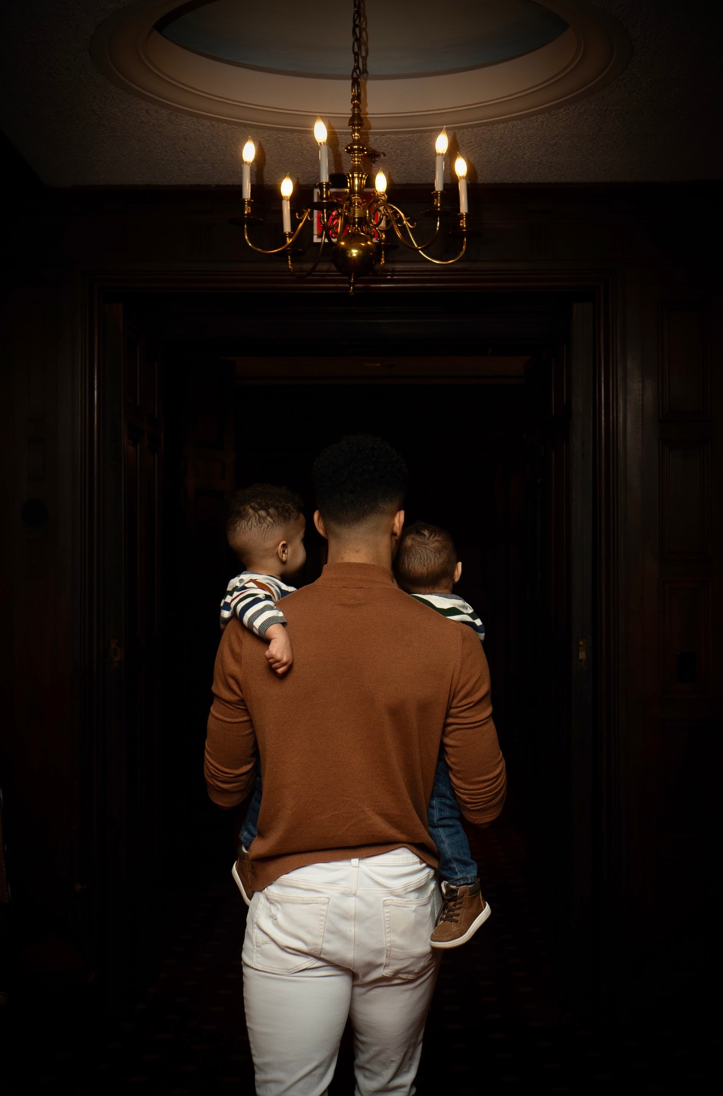 Family portrait, father carrying two sons under chandelier, cinematic silhouette